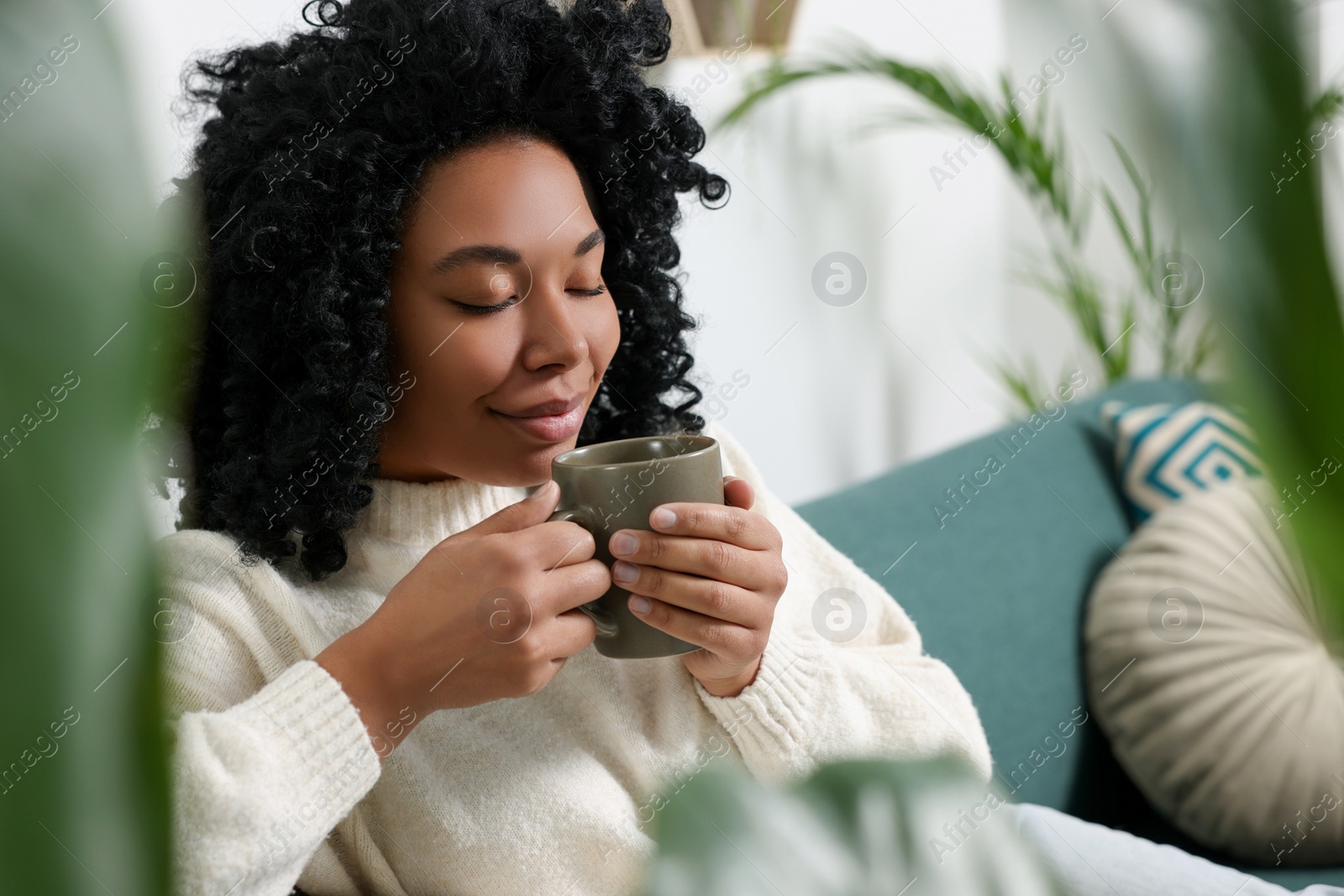 Photo of Relaxing atmosphere. Woman with cup of hot drink near beautiful houseplants indoors