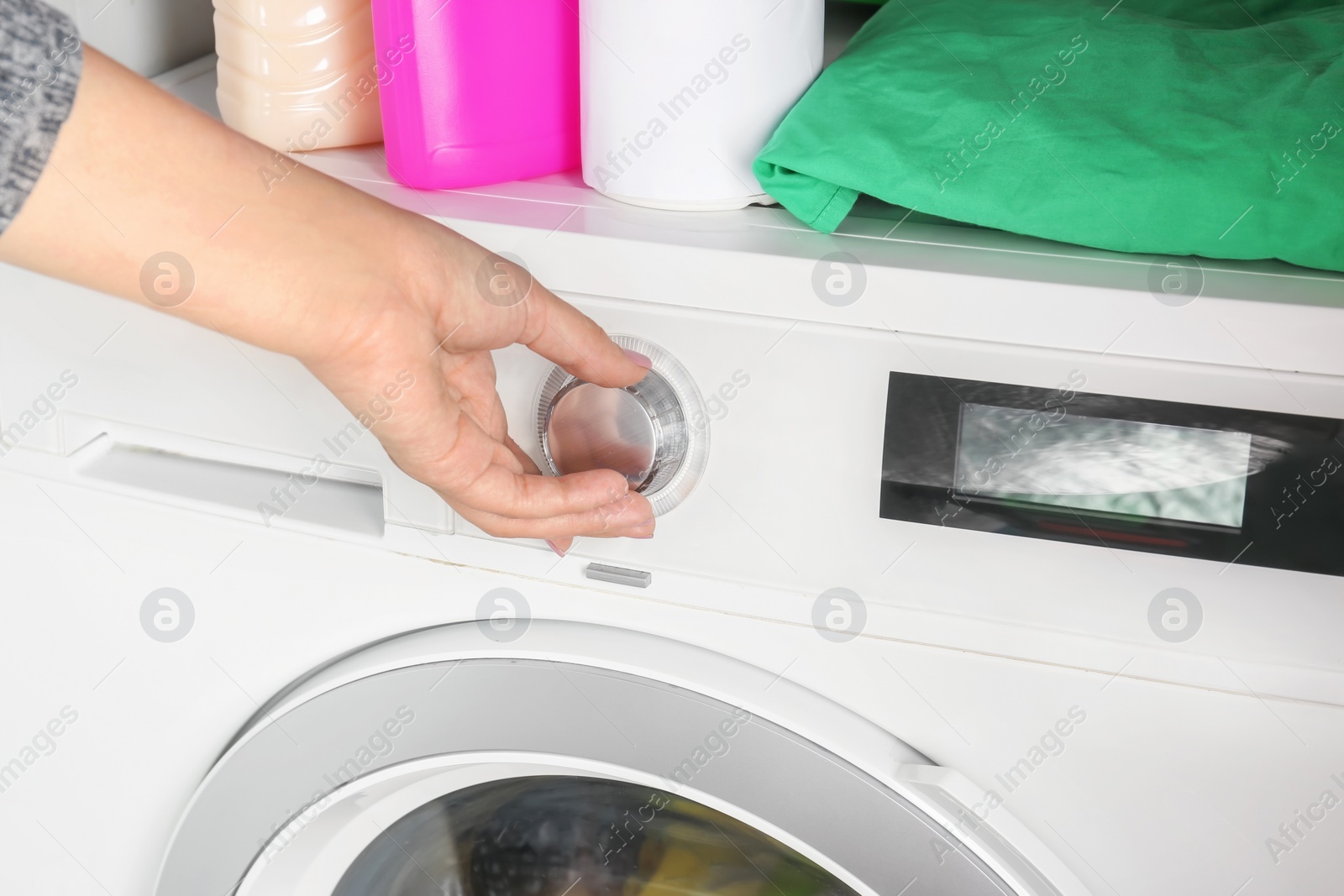 Photo of Young woman turning regulator on washing machine, closeup