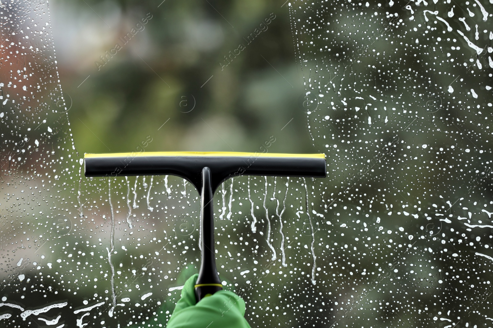 Photo of Woman cleaning glass with squeegee indoors, closeup