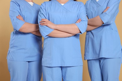 Photo of Nurses in medical uniforms on light brown background, closeup