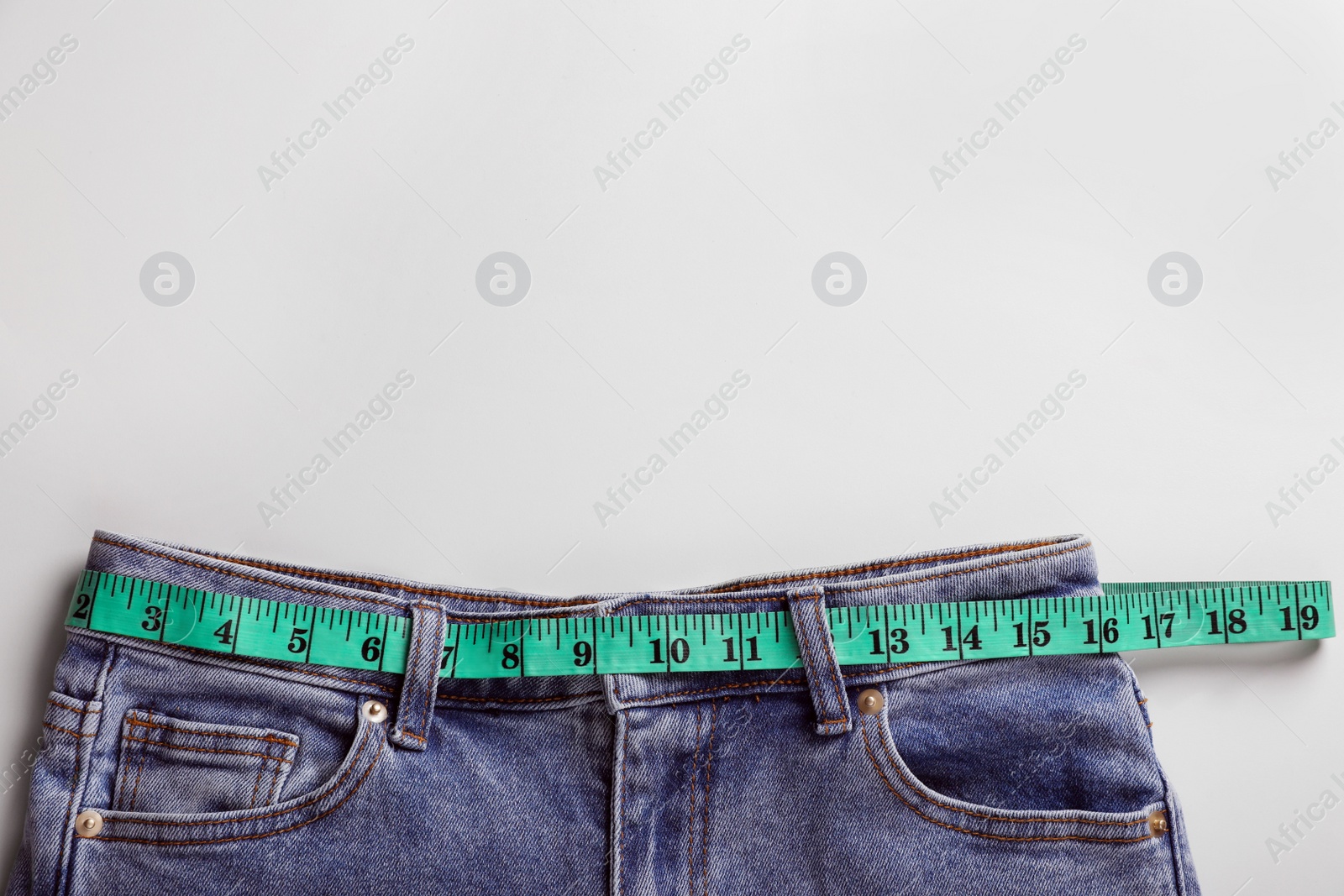 Photo of Jeans with measuring tape on light grey background, top view and space for text. Weight loss concept