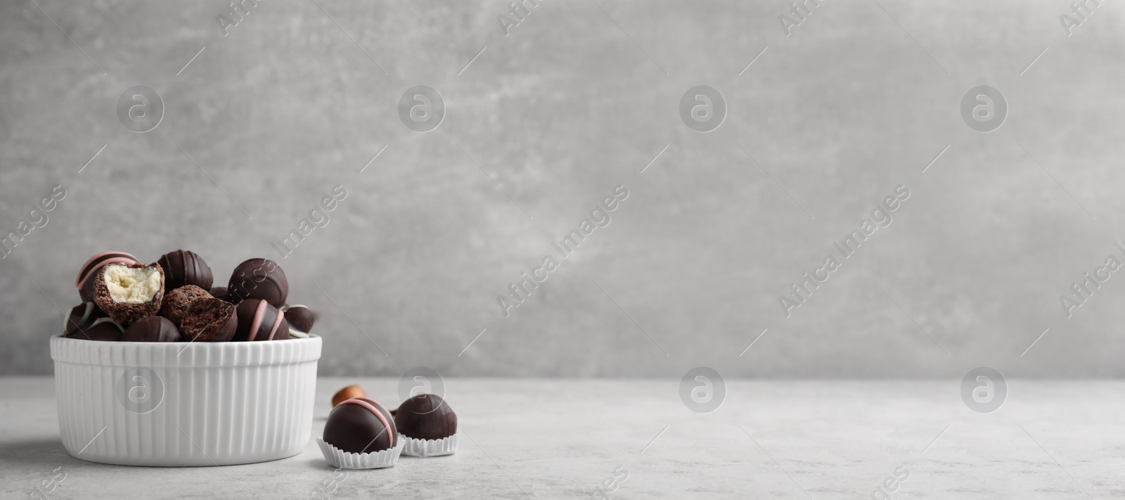 Photo of Different delicious chocolate truffles in bowl on light grey table. Space for text