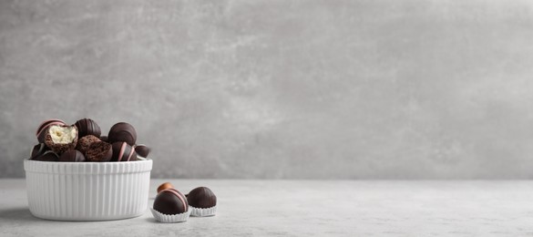 Photo of Different delicious chocolate truffles in bowl on light grey table. Space for text