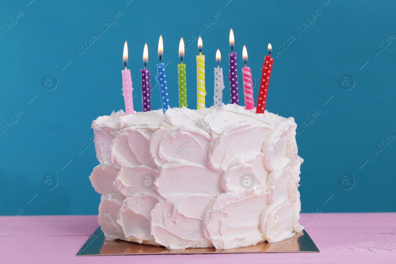 Photo of Delicious cake with cream and burning candles on pink wooden table