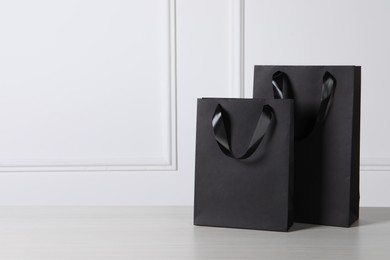 Black paper bags on white wooden table, space for text