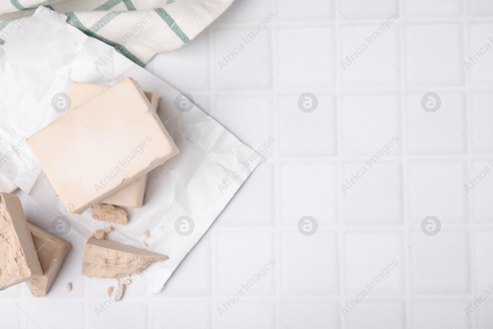 Photo of Blocks of compressed yeast on white tiled table, flat lay. Space for text