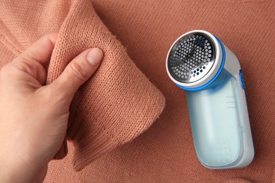 Photo of Woman holding sleeve of sweater with lint and fabric shaver, top view