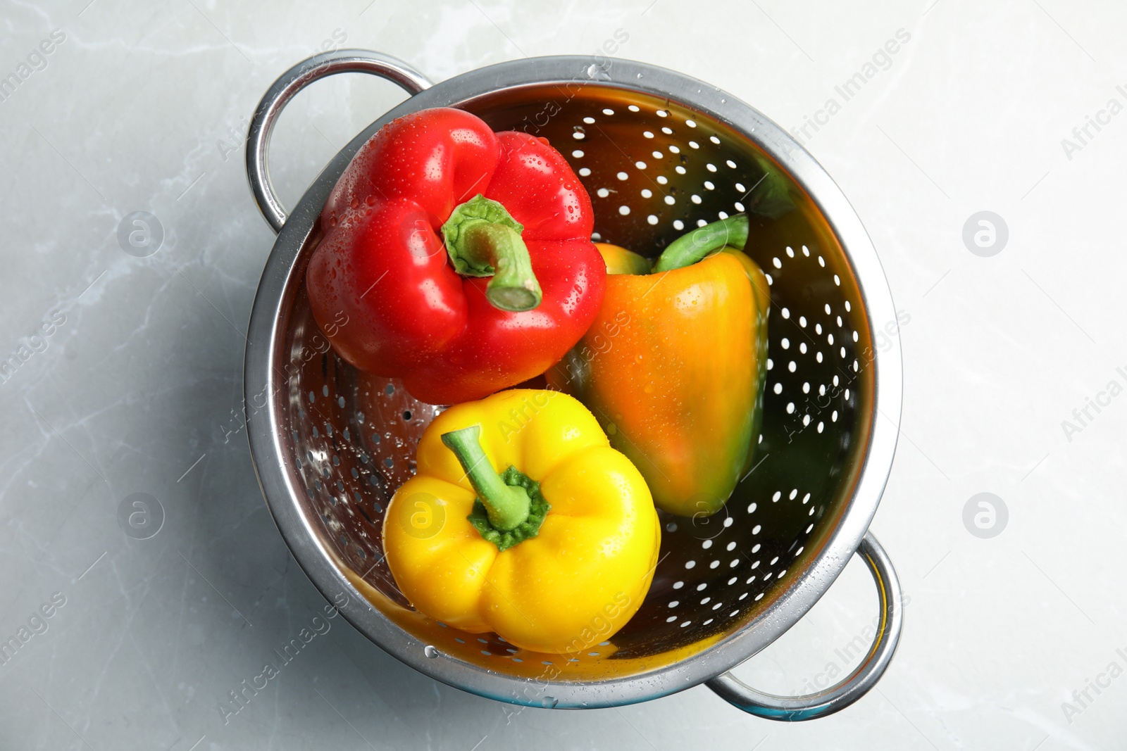 Photo of Colander with ripe paprika peppers on grey  background, top view