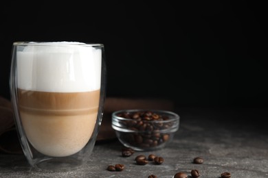 Photo of Delicious latte macchiato and coffee beans on grey table, space for text