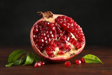 Photo of Cut fresh pomegranate and green leaves on wooden table, closeup