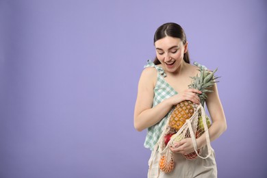 Woman with string bag of fresh fruits on violet background, space for text