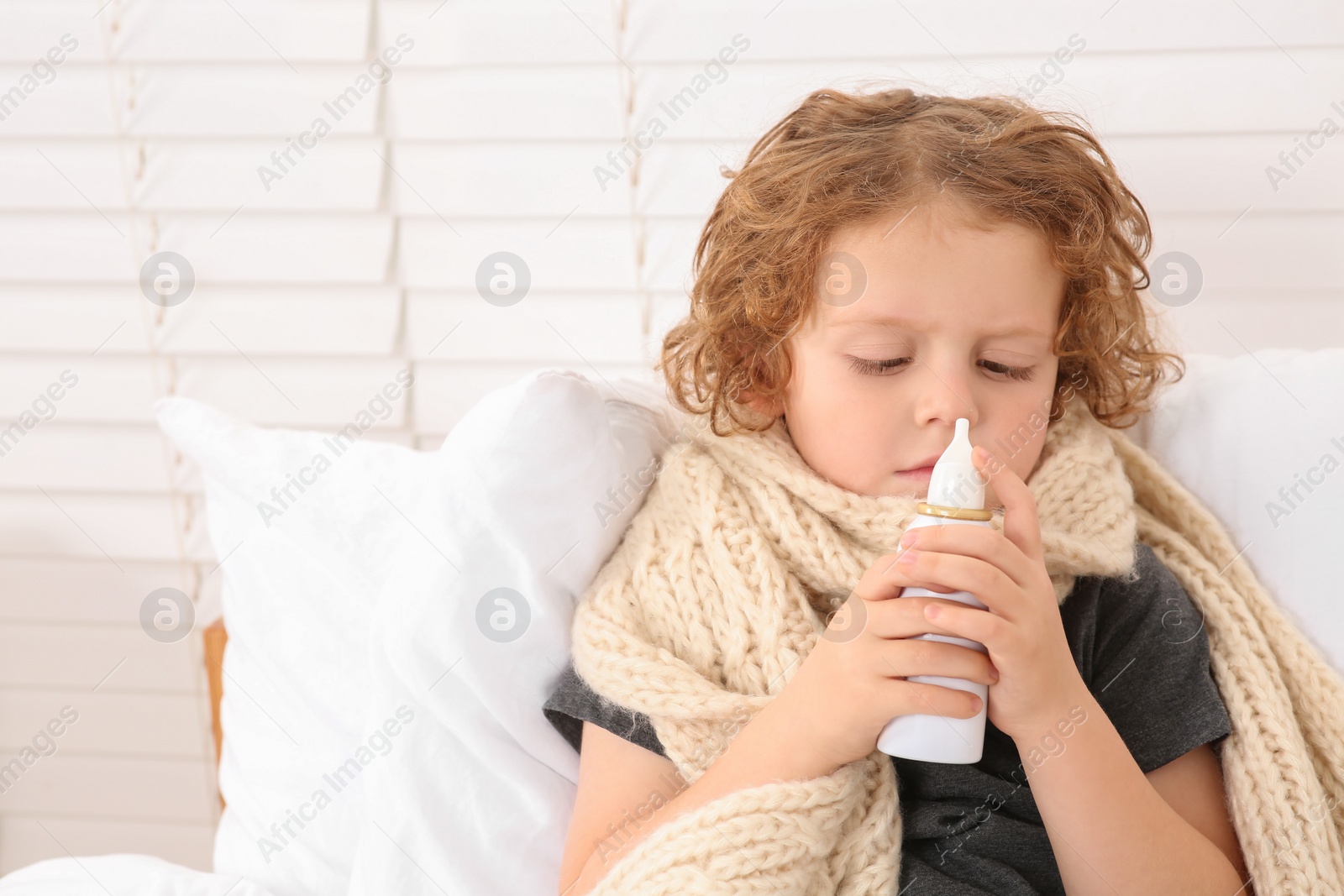 Photo of Cute little boy using nasal spray on bed indoors, space for text