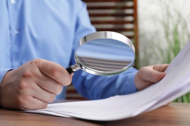 Man looking at document through magnifier at wooden table, closeup. Searching concept