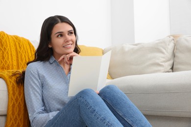 Young woman with greeting card on floor in living room, space for text