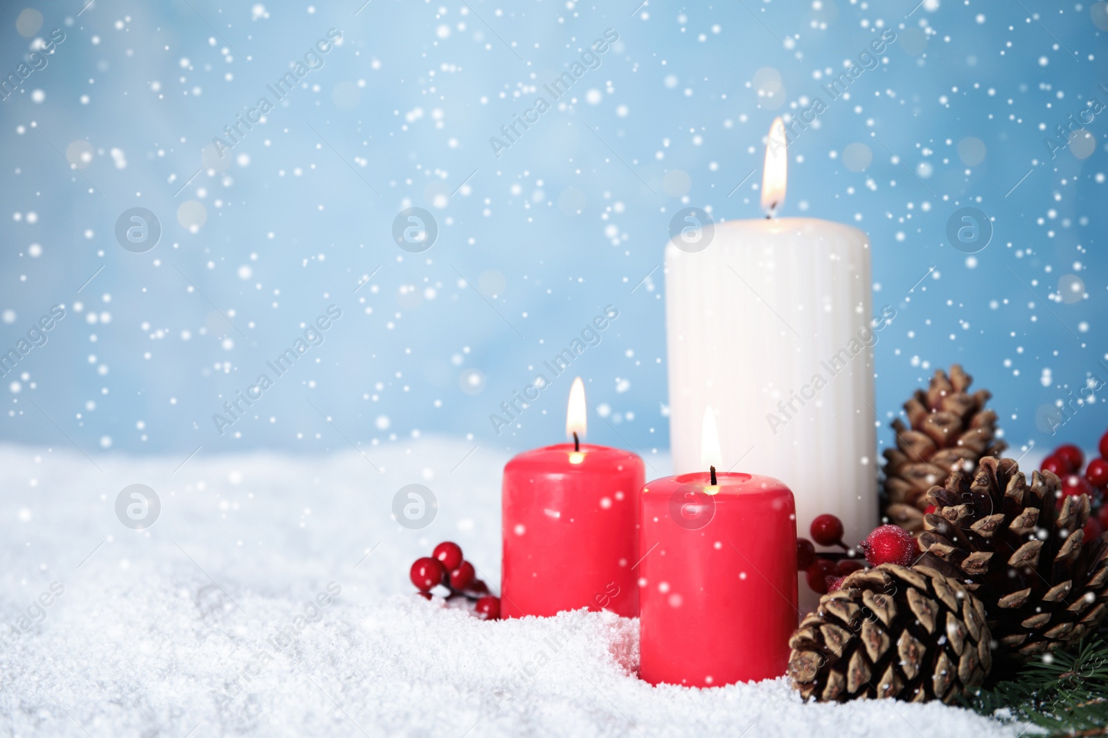 Photo of Snow falling on burning candles and pine cones against light blue background, space for text. Christmas eve