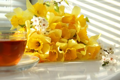 Photo of Yellow daffodils and beautiful white flowers of plum tree on windowsill, closeup