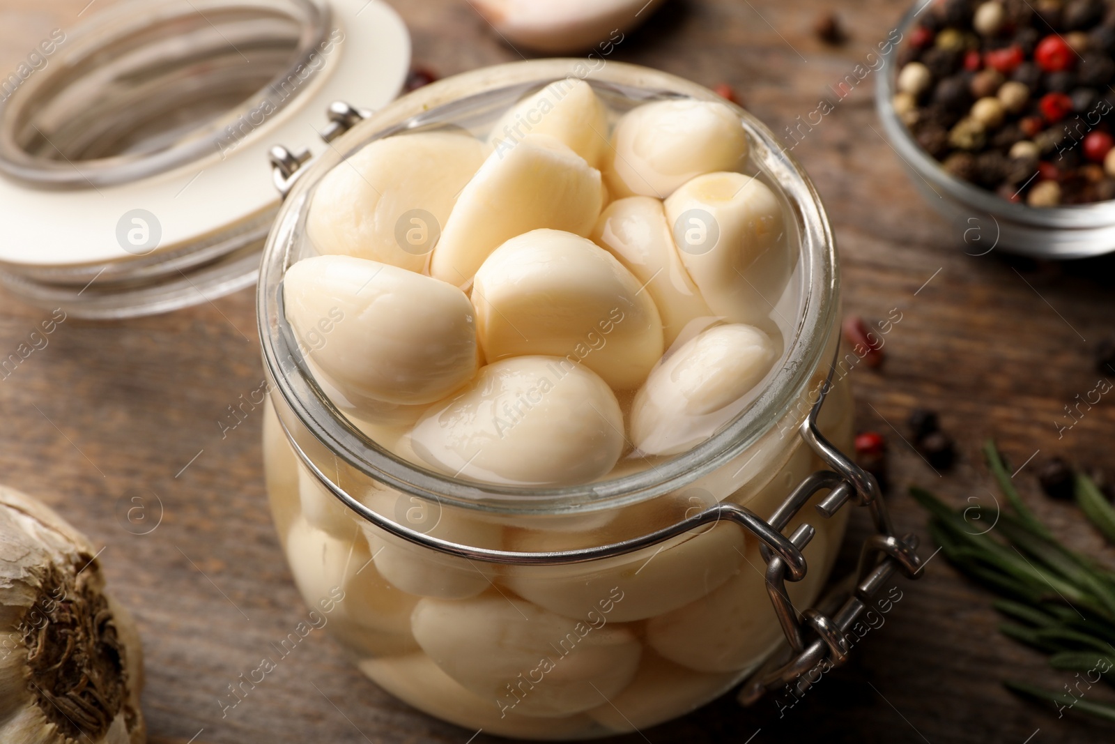 Photo of Preserved garlic in glass jar on wooden table, closeup