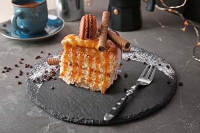 Photo of Piece of delicious homemade cake with caramel sauce and macaron on table