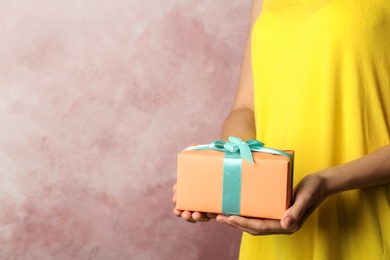 Woman holding beautifully wrapped gift box on color background