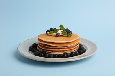 Photo of Stack of tasty pancakes with blueberries, butter and mint on light blue background