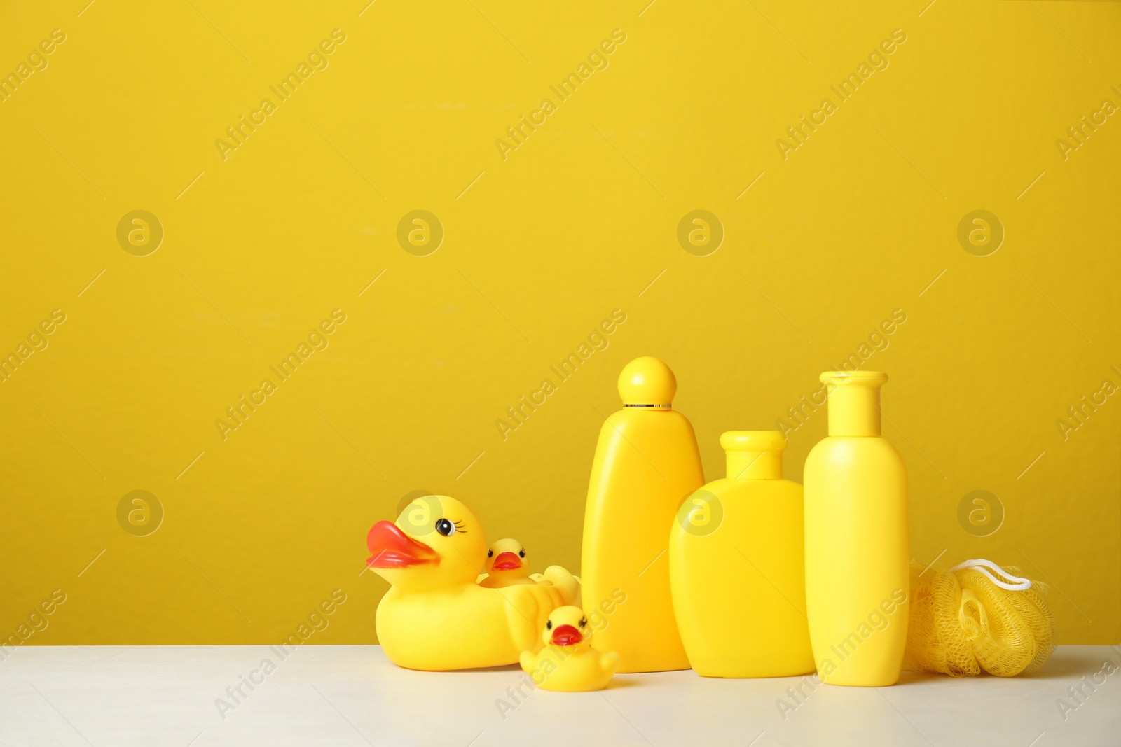 Photo of Baby cosmetic products, toys and accessories on white table against yellow background. Space for text