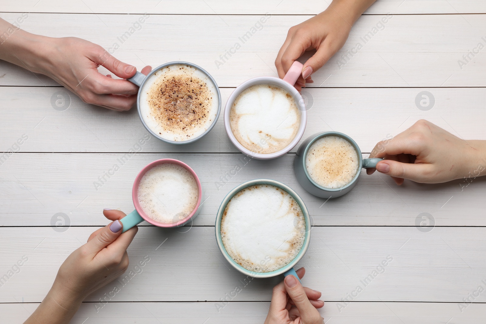 Photo of People holding different cups with aromatic hot coffee at white wooden table, top view