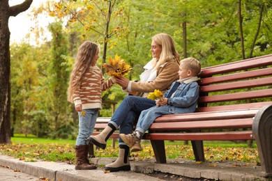 Photo of Happy mother and her children spending time together with dry leaves in autumn park