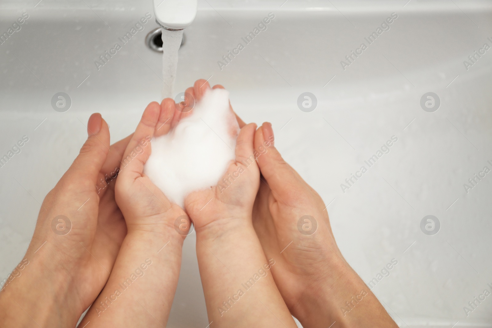 Photo of Mother and daughter washing hands in bathroom at home, closeup