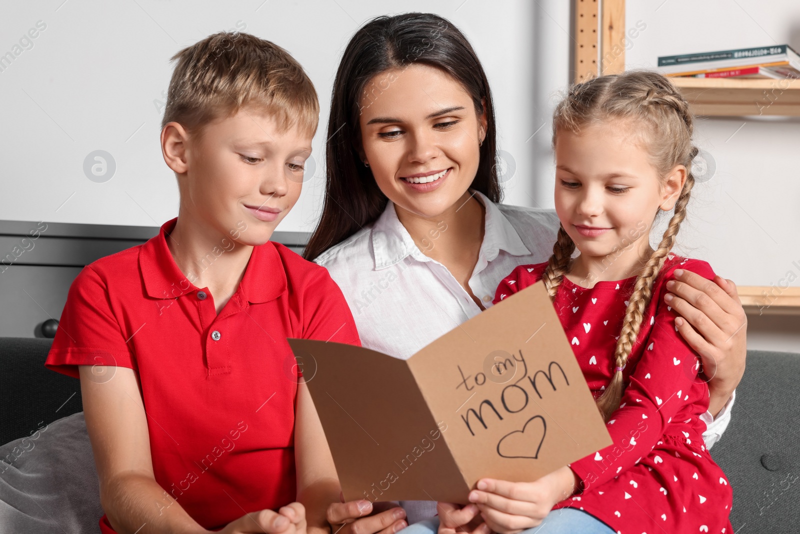 Photo of Happy woman receiving greeting card from her children at home