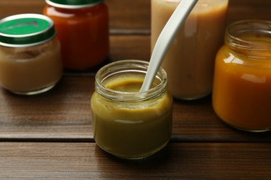 Tasty baby food in jars on wooden table
