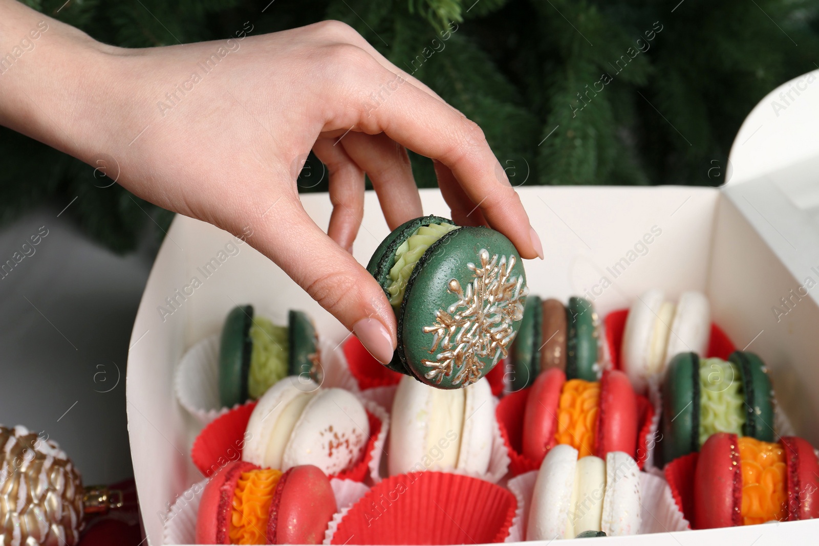 Photo of Woman with box of decorated Christmas macarons at table, closeup