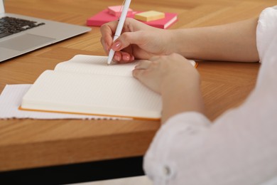 Woman writing in notebook at wooden table indoors, closeup