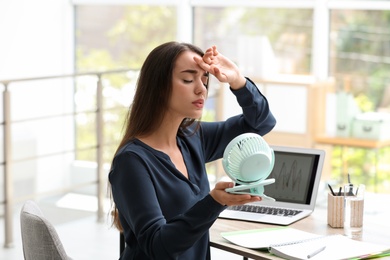 Photo of Woman with portable fan suffering from heat at workplace. Summer season