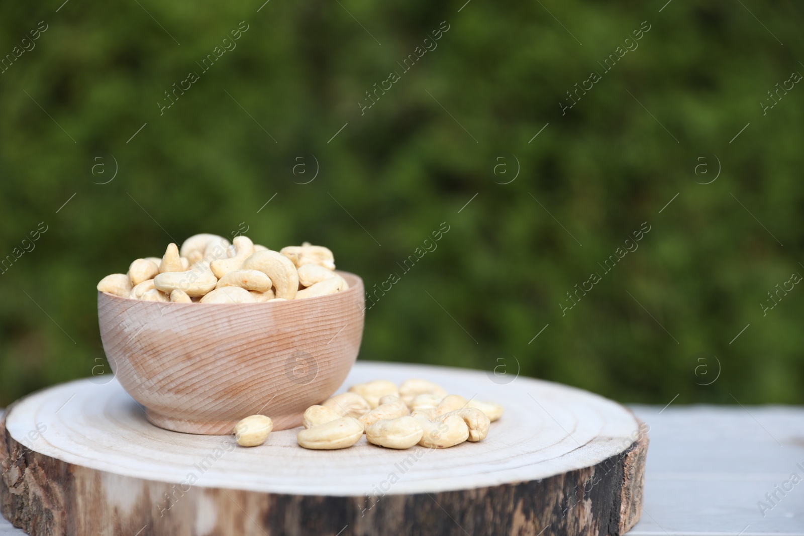 Photo of Tasty cashew nuts in bowl on table outdoors, space for text