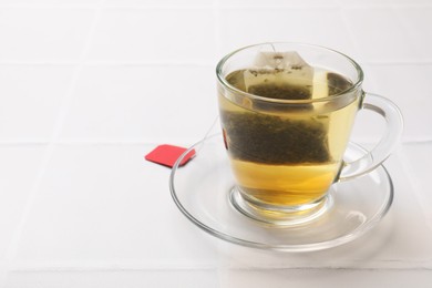 Tea bag in cup with hot drink on white tiled table. Space for text