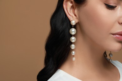 Photo of Young woman wearing elegant pearl earrings on brown background, closeup. Space for text