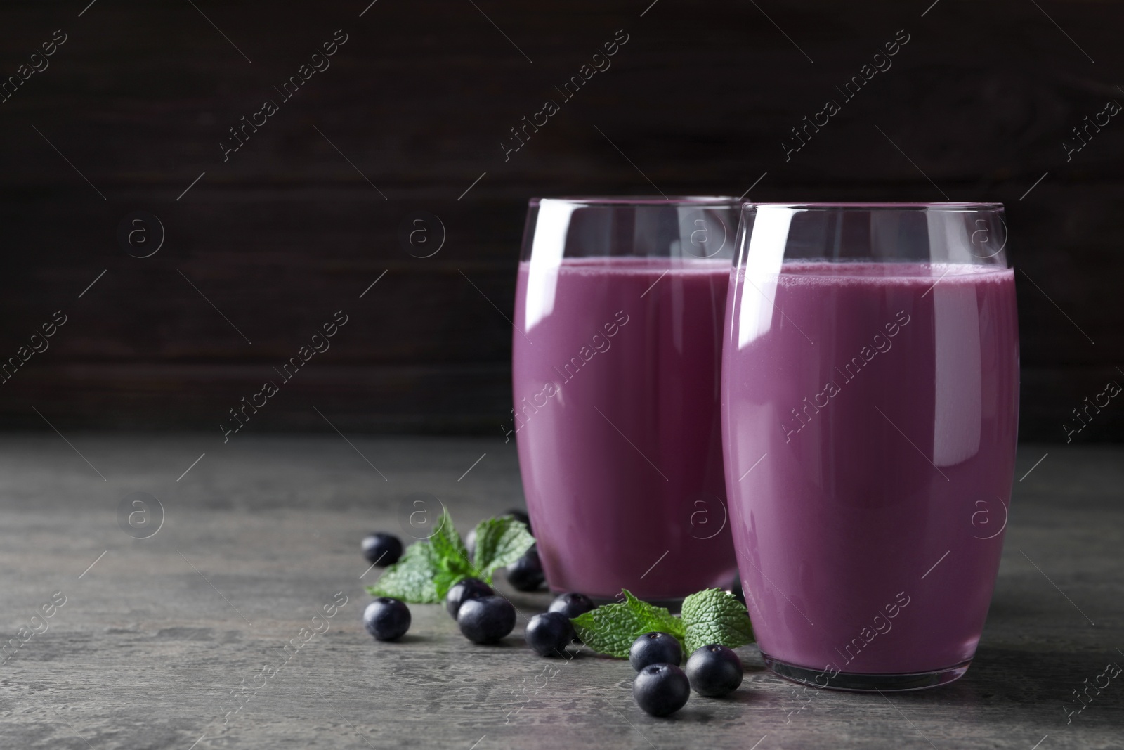 Photo of Tasty acai drink in glasses and berries on grey table, space for text