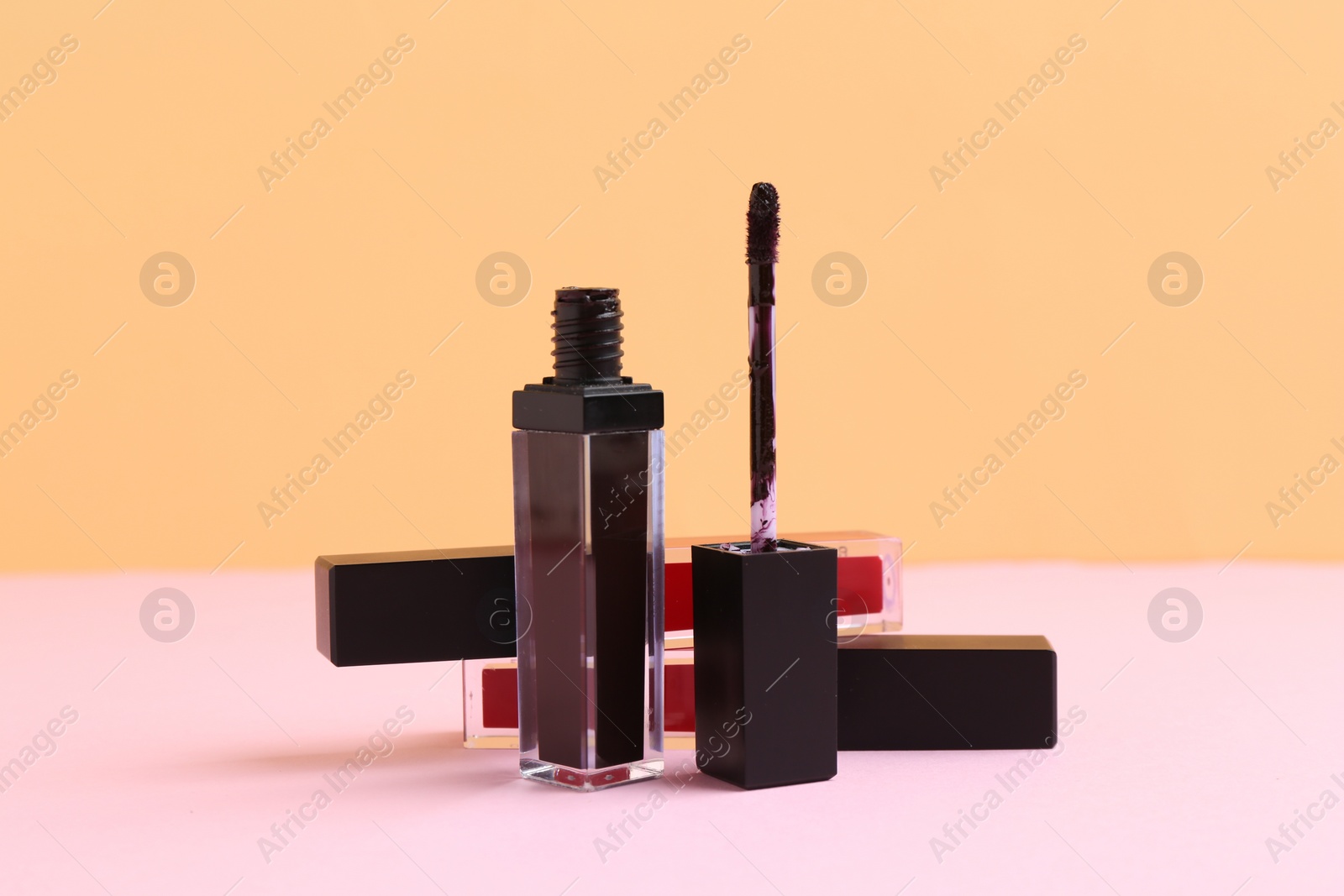 Photo of Different lip glosses and applicator on color background