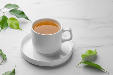 Photo of Green tea in cup with saucer and leaves on white marble table
