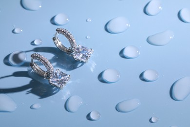 Luxury jewelry. Elegant earrings on light blue surface covered with water drops, space for text