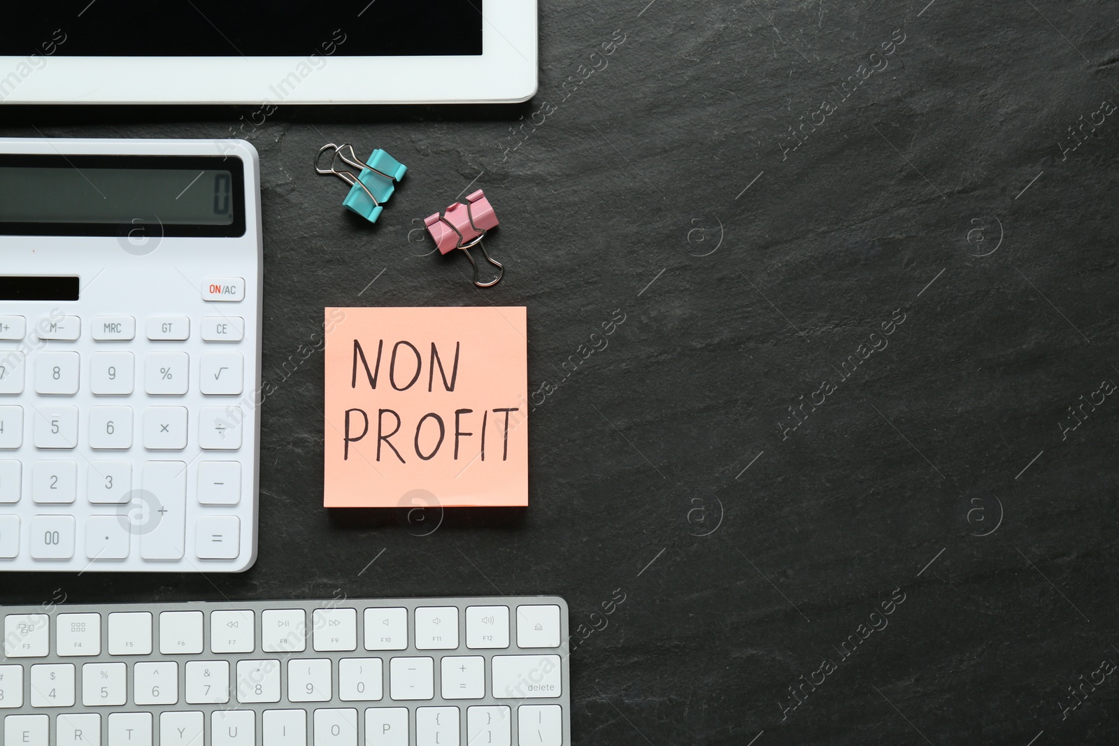 Photo of Paper note with Non Profit calculator and computer keyboard on black table, flat lay. Space for text