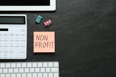Photo of Paper note with Non Profit calculator and computer keyboard on black table, flat lay. Space for text