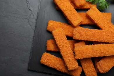 Fresh breaded fish fingers served on black table, top view