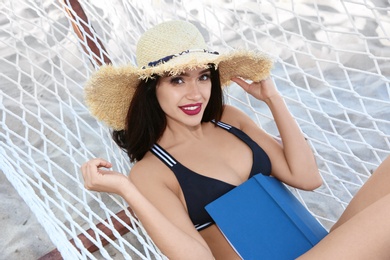 Young woman with book resting in hammock at seaside. Summer vacation