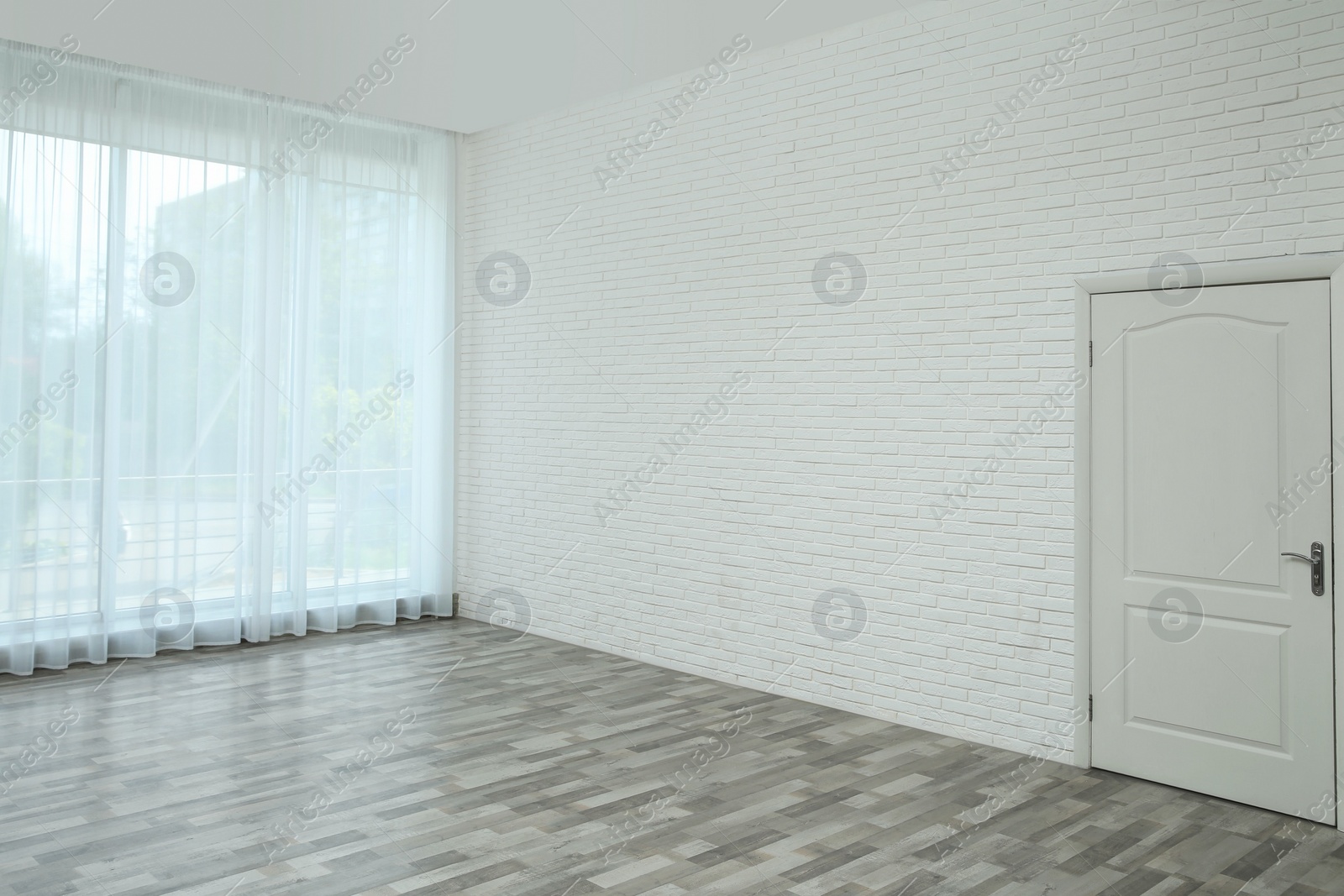 Photo of Empty room with brick wall, large window and white door