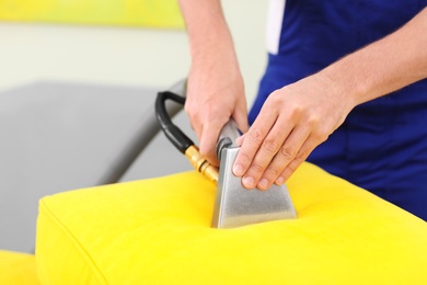 Photo of Dry cleaning worker removing dirt from sofa cushion indoors