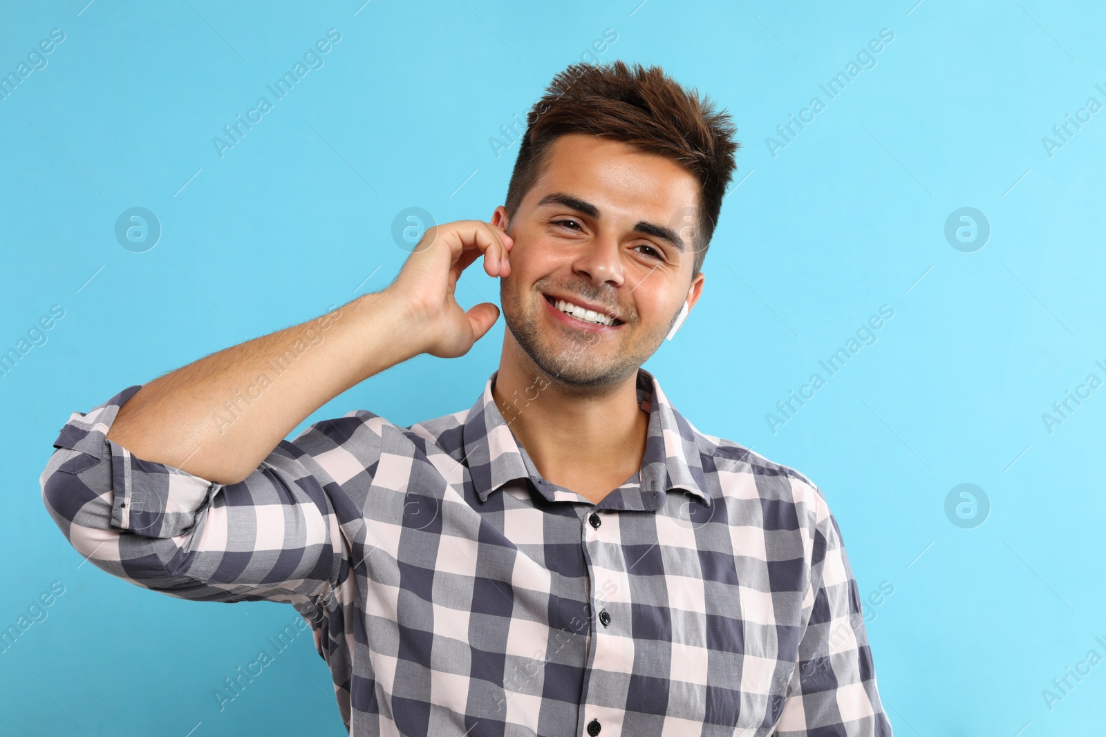 Photo of Happy young man listening to music through wireless earphones on light blue background