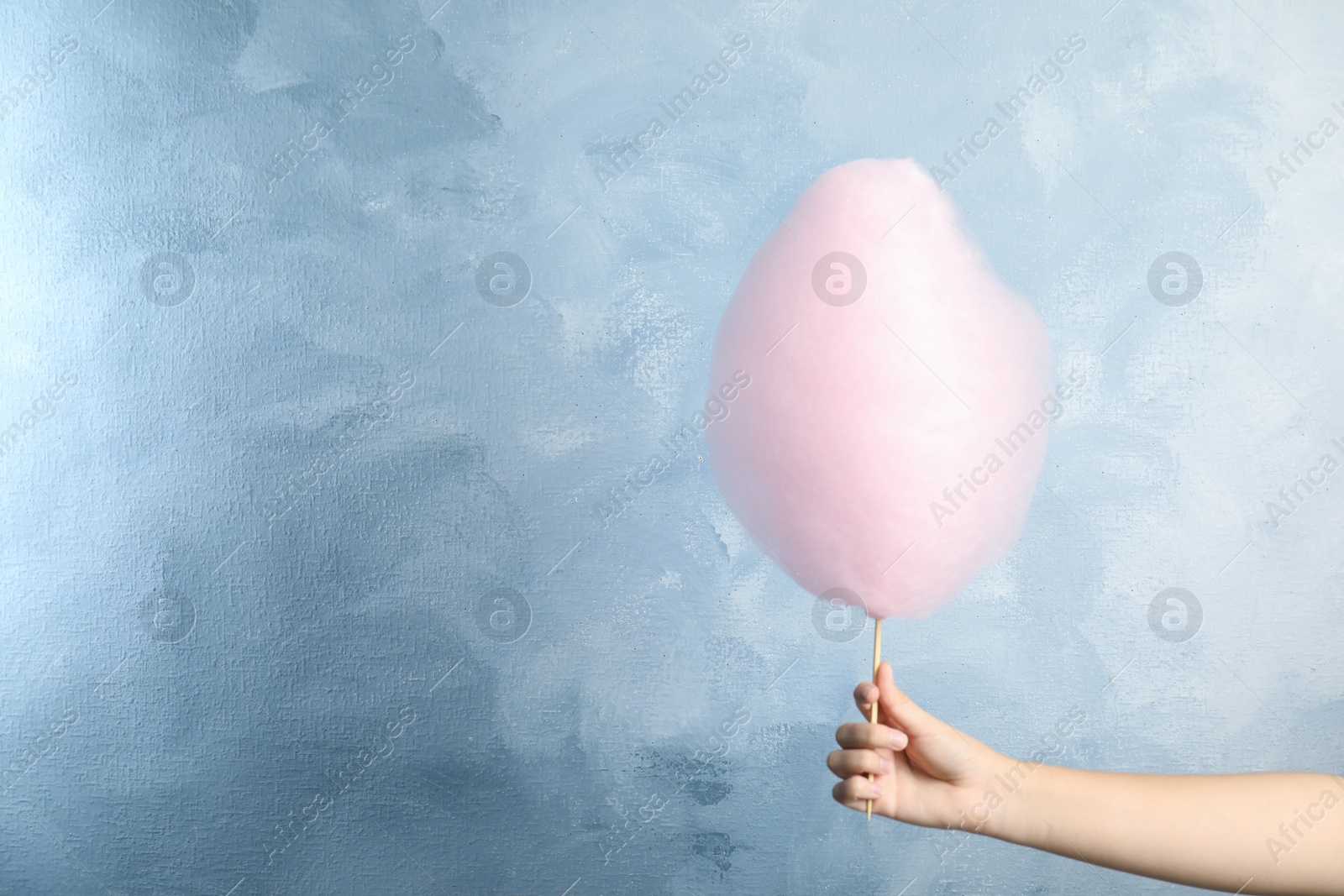 Photo of Woman holding sweet pink cotton candy on light blue background, closeup view. Space for text