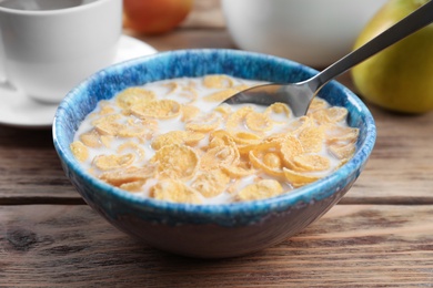 Photo of Healthy cornflakes with milk in bowl served on wooden table, closeup