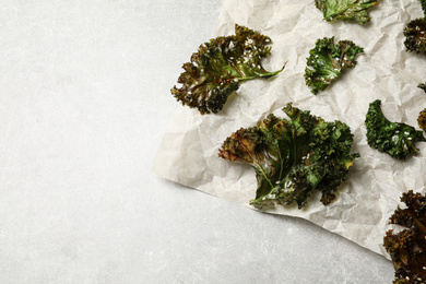 Photo of Tasty baked kale chips on grey table, flat lay. Space for text